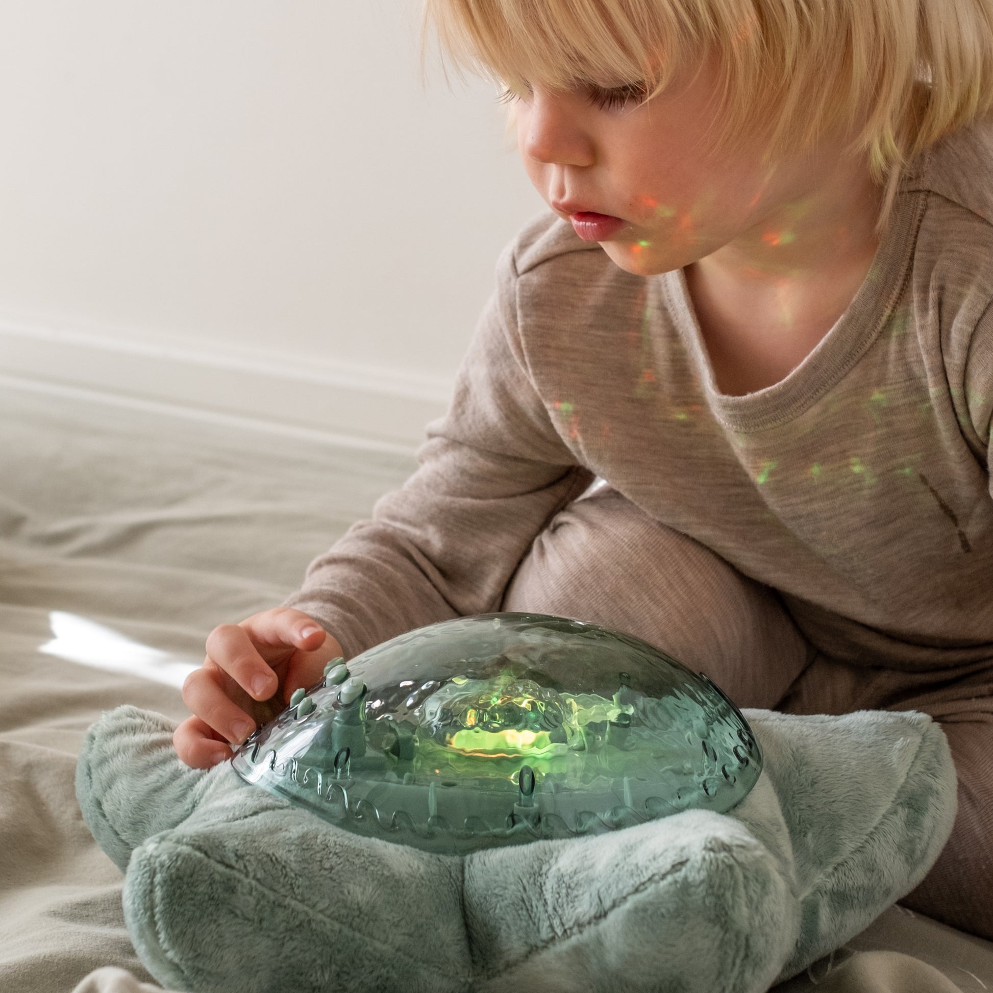 Child holding a glowing green sound machine with a soft focus background